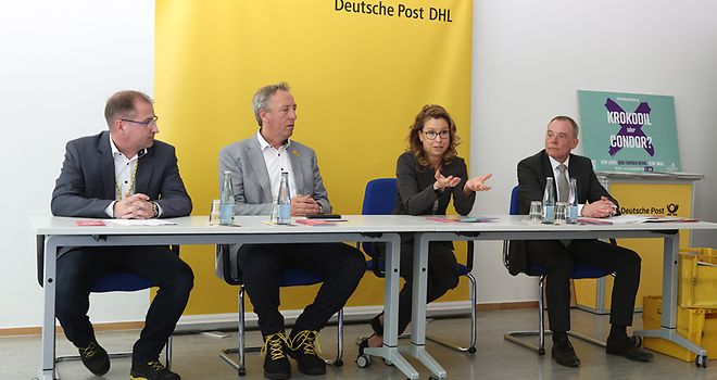 Carola Veit sowie Oliver Rudolf und zwei Mitarbeiter von DHL sitzen an einem Tisch und reden über die Wahlmotivationskampagne.