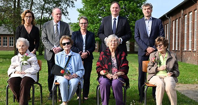 Foto von einer Personengruppe, die ehemaligen KZ-Häftlinge sitzen in der vorderen Reihe auf Stühlen, dahinter stehen die weiteren Personen.