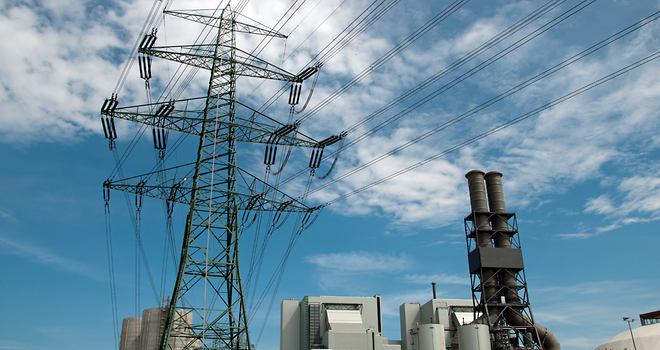 Ein Kraftwerk mit Schornsteinen und ein hoher Strommast unter einem blauen Himmel mit Wolken.