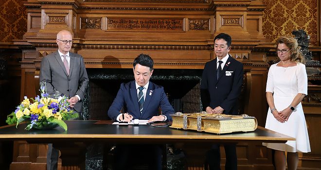 Der Bürgermeister von Osaka trägt sich in das Goldene Buch ein. Dr. Peter Tschentscher, Carola Veit und der Parlamentspräsident von Osaka stehen daneben.